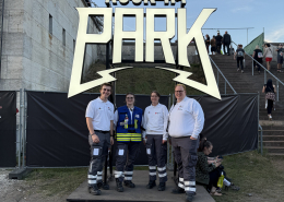 4 ehrenamtliche EInsatzkräfte des BRKs stehen vor dem Rock im Park Logo-Schild.
